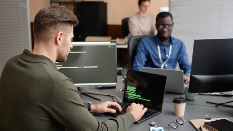 Two men collaborating on computers in a modern office setting, focused on Cyber Security Courses