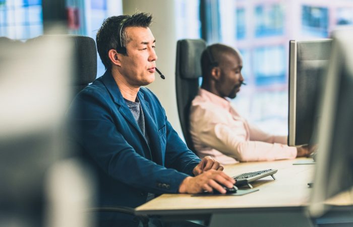 A man seated at a desk, focused on his computer screen, with papers and a pen nearby.