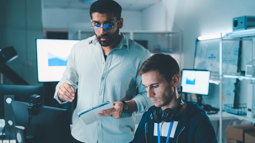 Two men collaborating on a computer in a modern office setting, focused on their work.