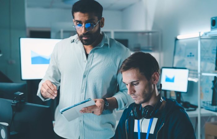 Two men collaborating on a computer in a modern office setting, focused on their work.